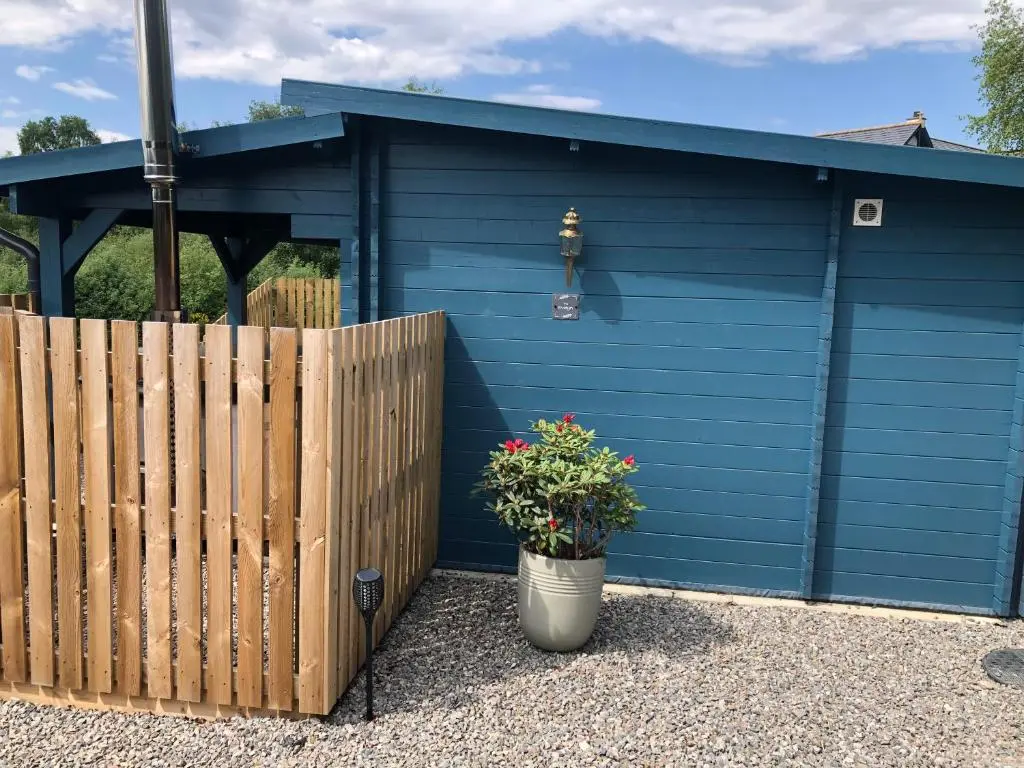 a blue garage with a fence and a potted plant at Retreat Hot Tub Highland Cabin in Inverness