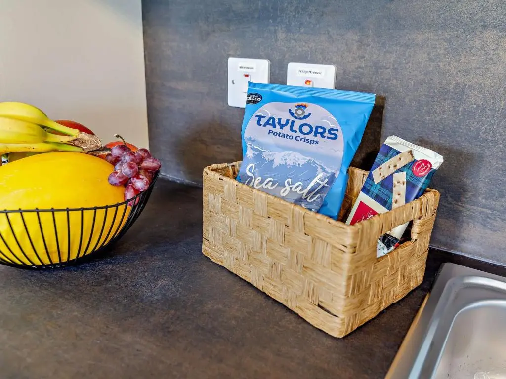 a basket of chips and a bag of chips and a bowl of fruit at 2 Bed in Kiltarlity 95056 in Kiltarlty