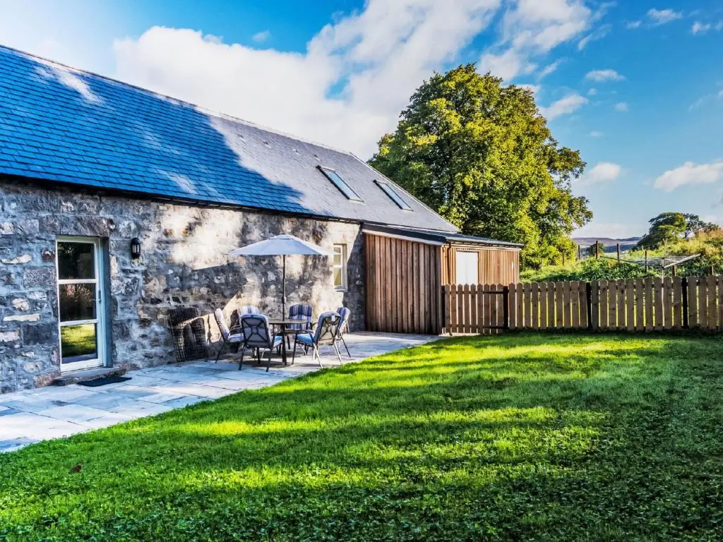 a stone cottage with a patio and grass yard at Holiday Home The Barn by Interhome in Drumnadrochit