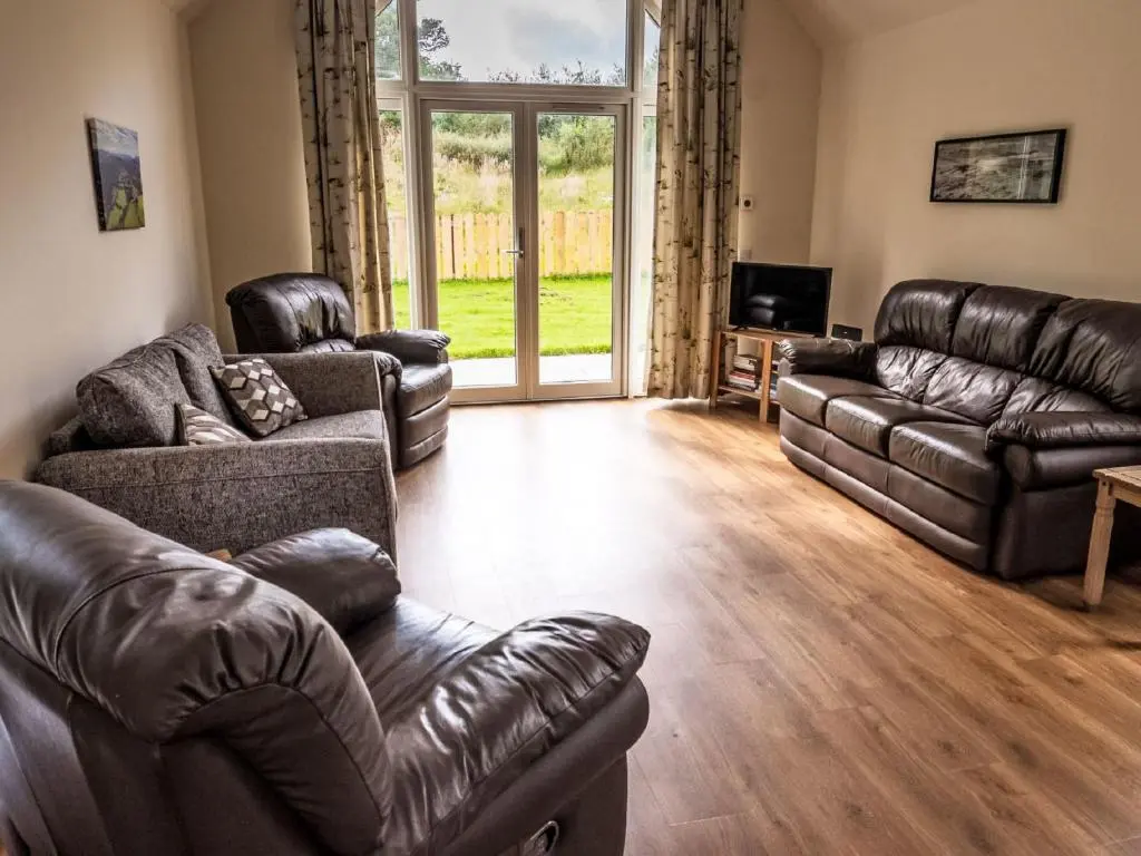 a living room with leather furniture and a large window at Holiday Home The Barn by Interhome in Drumnadrochit