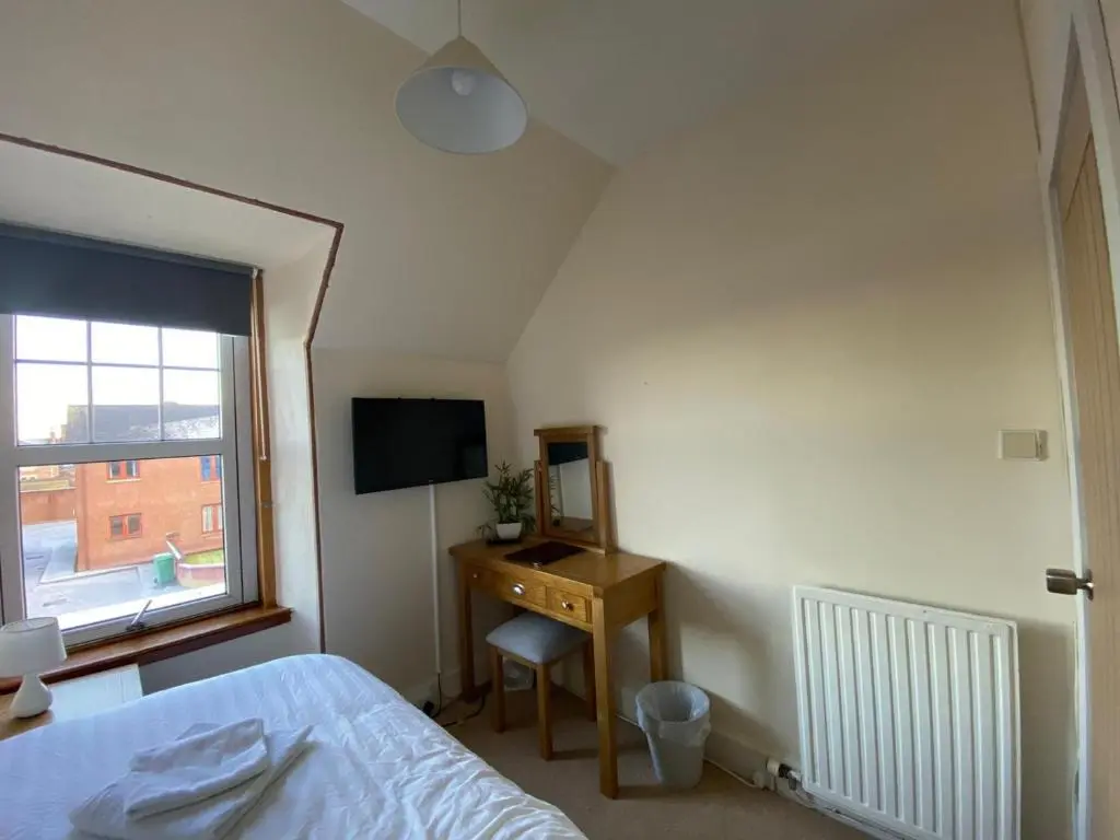 a bedroom with a bed and a desk and a window at Inverness Holiday House in Dalneigh