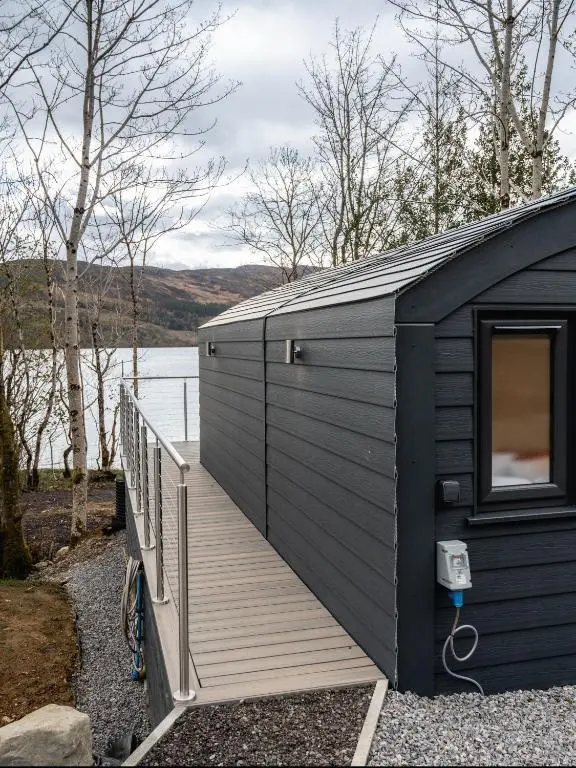 a black building with a deck next to a body of water at Alba Pod in Fort Augustus
