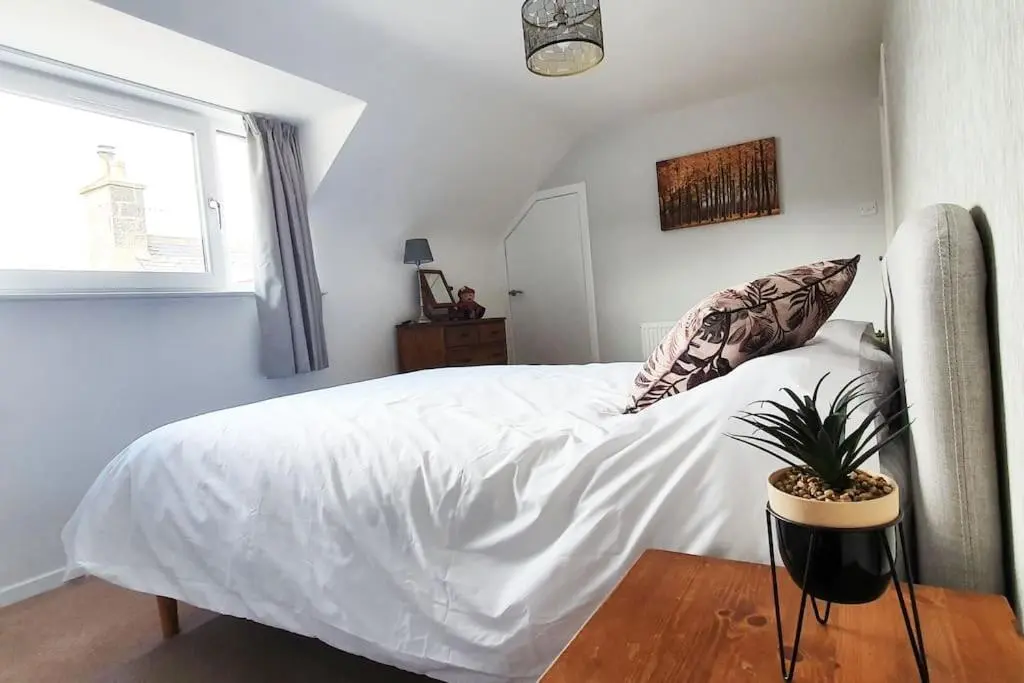 a bedroom with a white bed with a potted plant at York Street Retreat, modern cosy 2 bed with garden in Dufftown