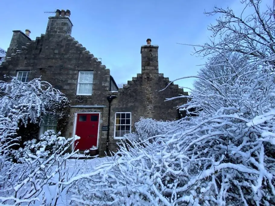a house with a red door covered in snow at Historical North Cottage in Old Deer in Old Deer