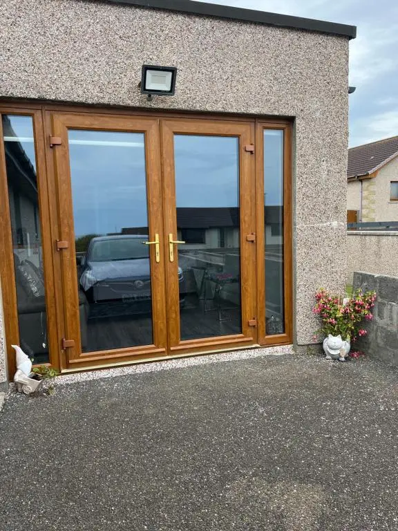 a house with wooden doors and windows with a car at Wee Coastal Snug in Wick