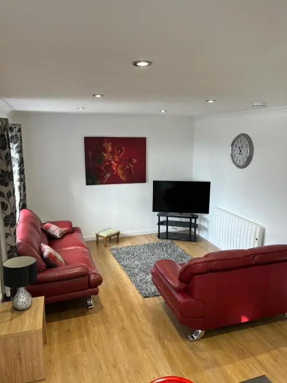 a living room with red leather furniture and a flat screen tv at Highland Holiday Lets Lairg in Lairg