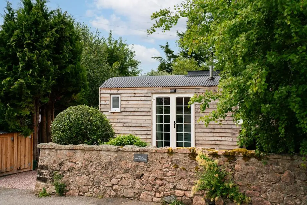 a small shed with a window and a stone wall at Willow's Nordic Shepherds Hut in Ballater