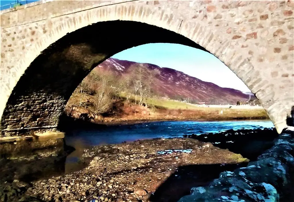 a bridge over a river with a mountain in the background at Selkie House Song of the Sea in Helmsdale