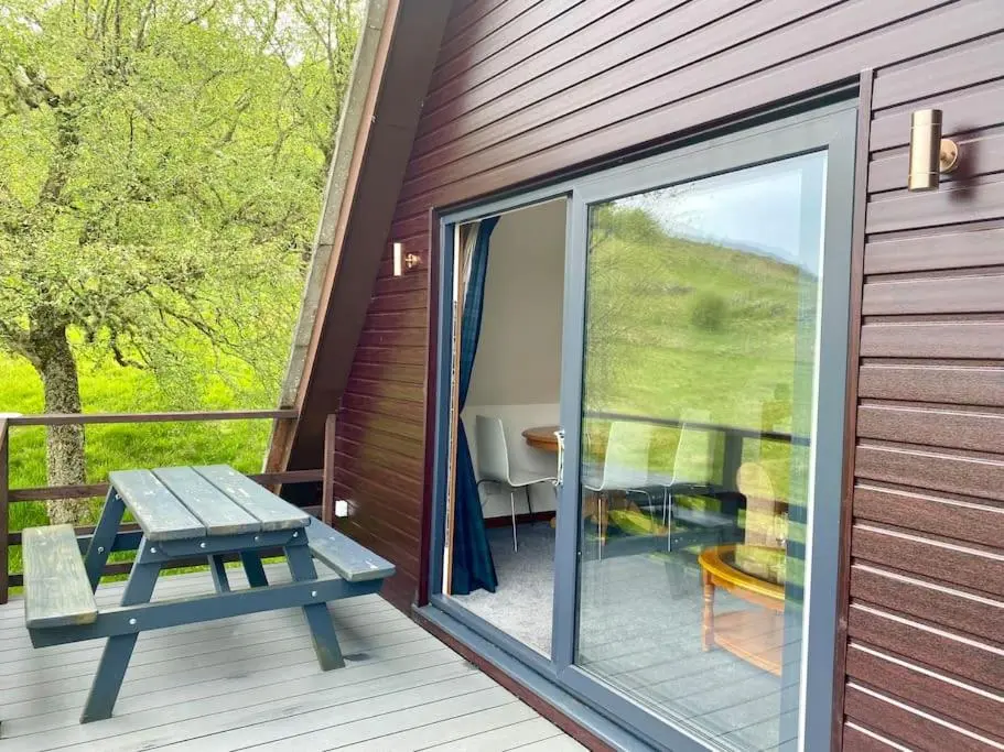 a wooden deck with a picnic table and a sliding glass door at Glen Lodges Rogart in Rogart