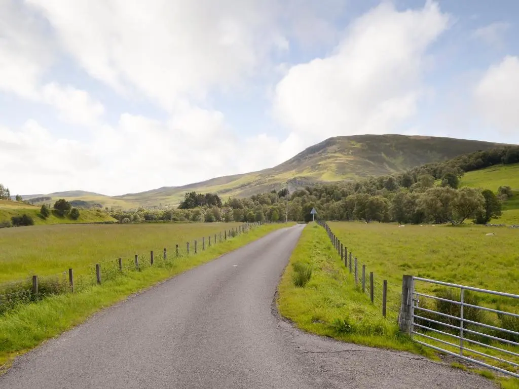 a road through a field with mountains in the background at Rowan Tree Cottage - S4216 in Tulchan