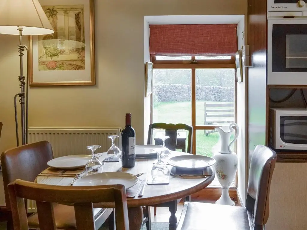 a dining room table with a bottle of wine on it at Rowan Tree Cottage - S4216 in Tulchan