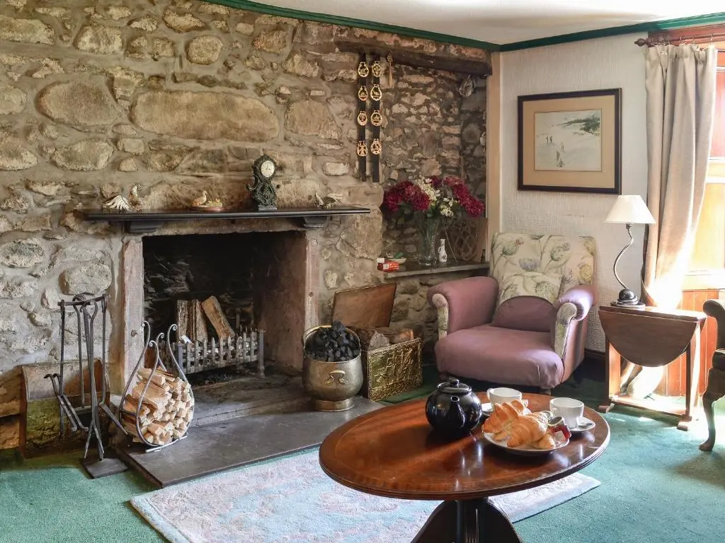 a living room with a table and a stone fireplace at Dalvanie Mill - S4241 in Tulchan