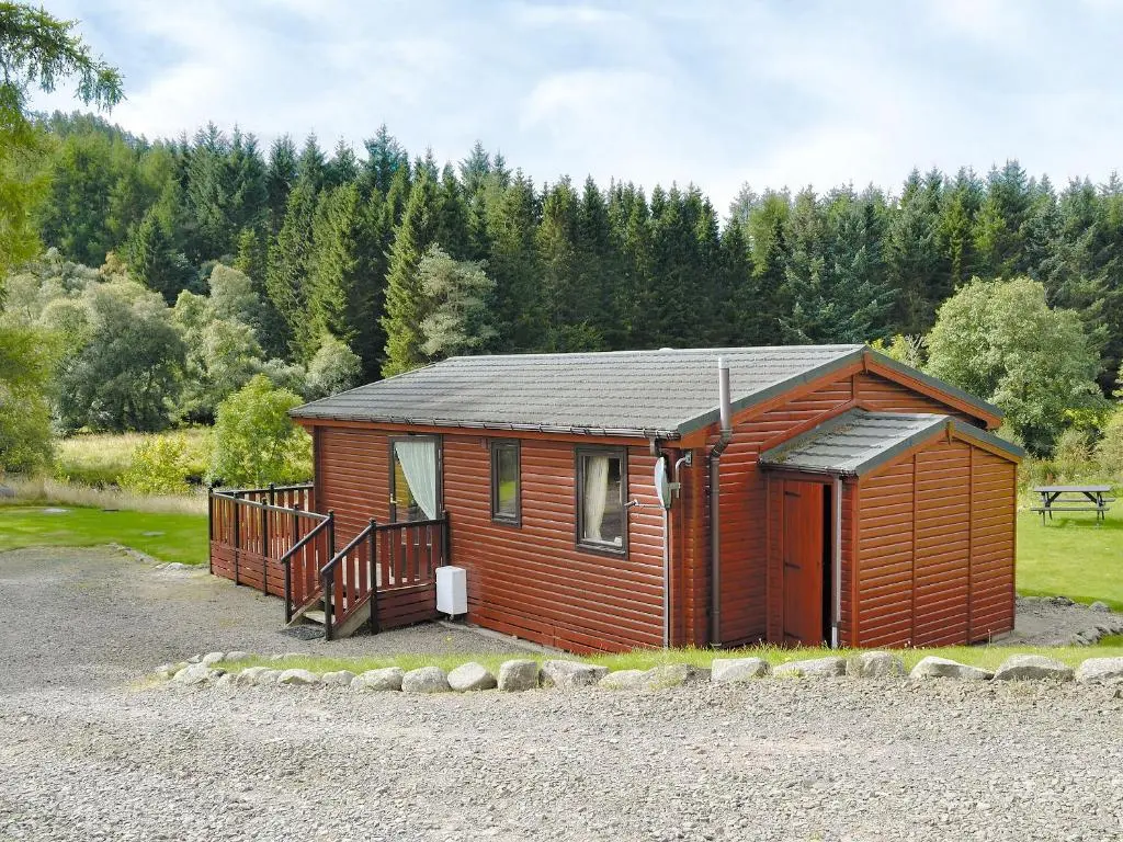 a small wooden cabin with a porch in a forest at Larch Cottage - S4428 in Kirkton of Glenisla