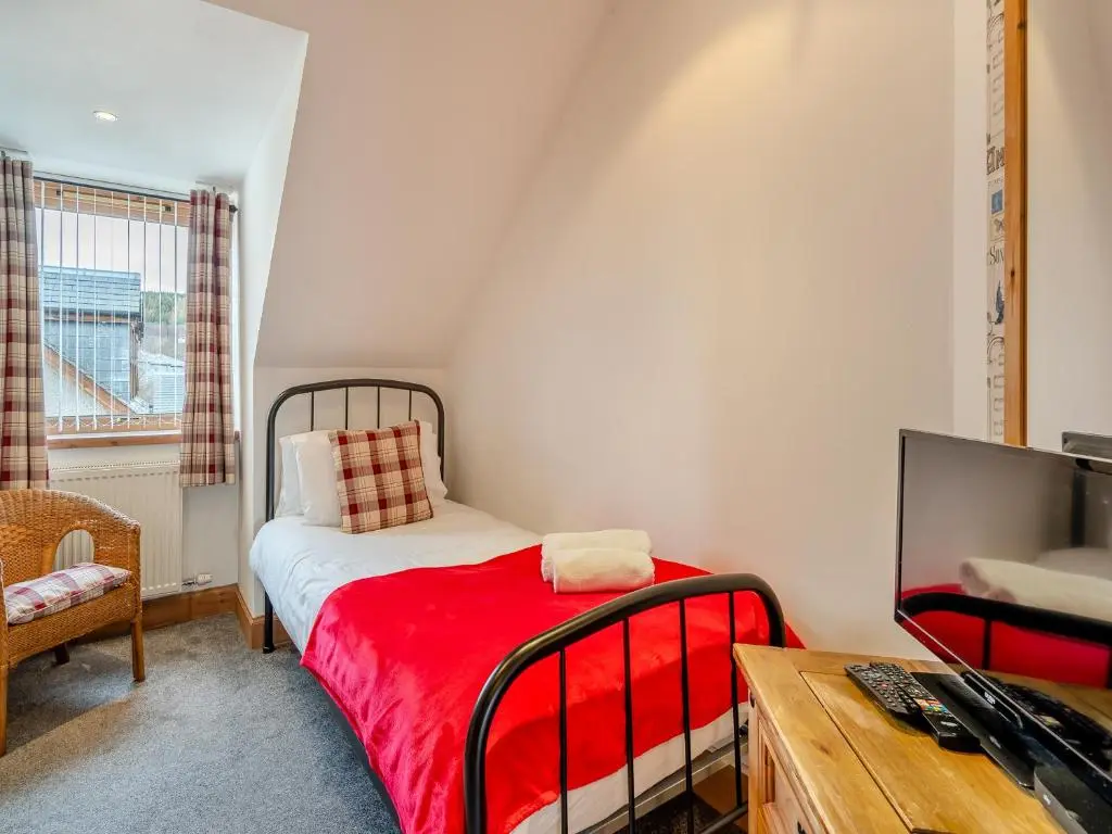 a small bedroom with a bed with a red blanket at Clunnie Mor - S4615 in Aviemore