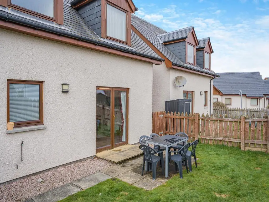 a patio with a table and chairs in front of a house at Clunnie Mor - S4615 in Aviemore