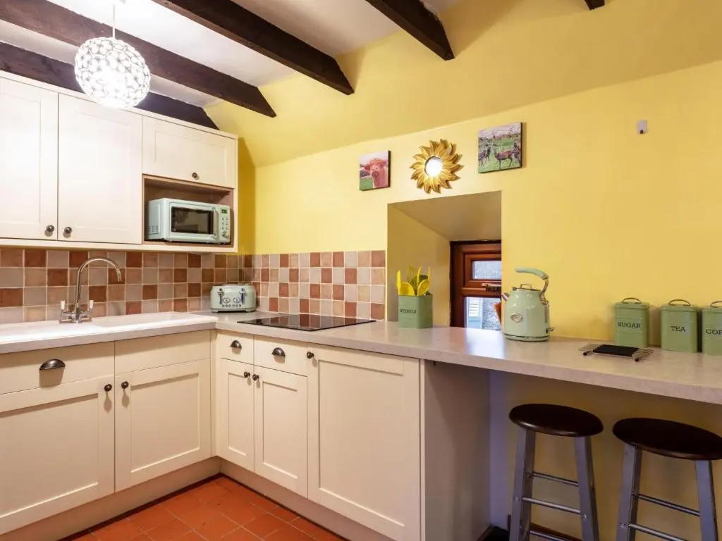a kitchen with white cabinets and a counter with stools at Holiday Home Sunflower Cottage by Interhome in Marnoch