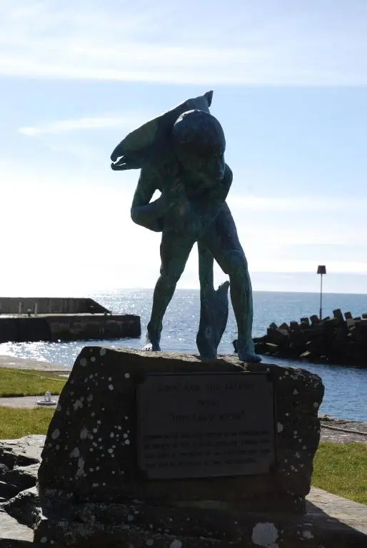 a statue of a person standing on a rock next to the ocean at Turadh 'a break in the clouds' in Dunbeath