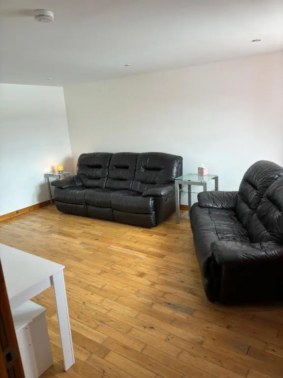 a living room with a black leather couch and a table at MacIver City Apartments Farraline Court in Inverness