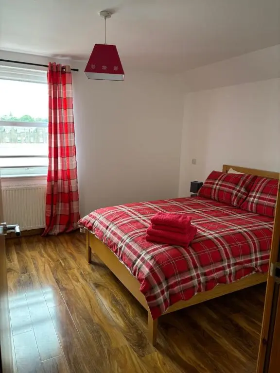 a bedroom with a bed with a red plaid blanket at MacIver City Apartments Farraline Court in Inverness