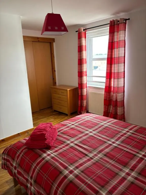 a bedroom with a red plaid bed and a window at MacIver City Apartments Farraline Court in Inverness