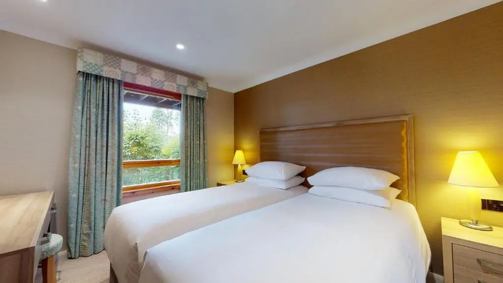 a bedroom with a large white bed and a window at The Lodges at Craigendarroch Country Club in Ballater