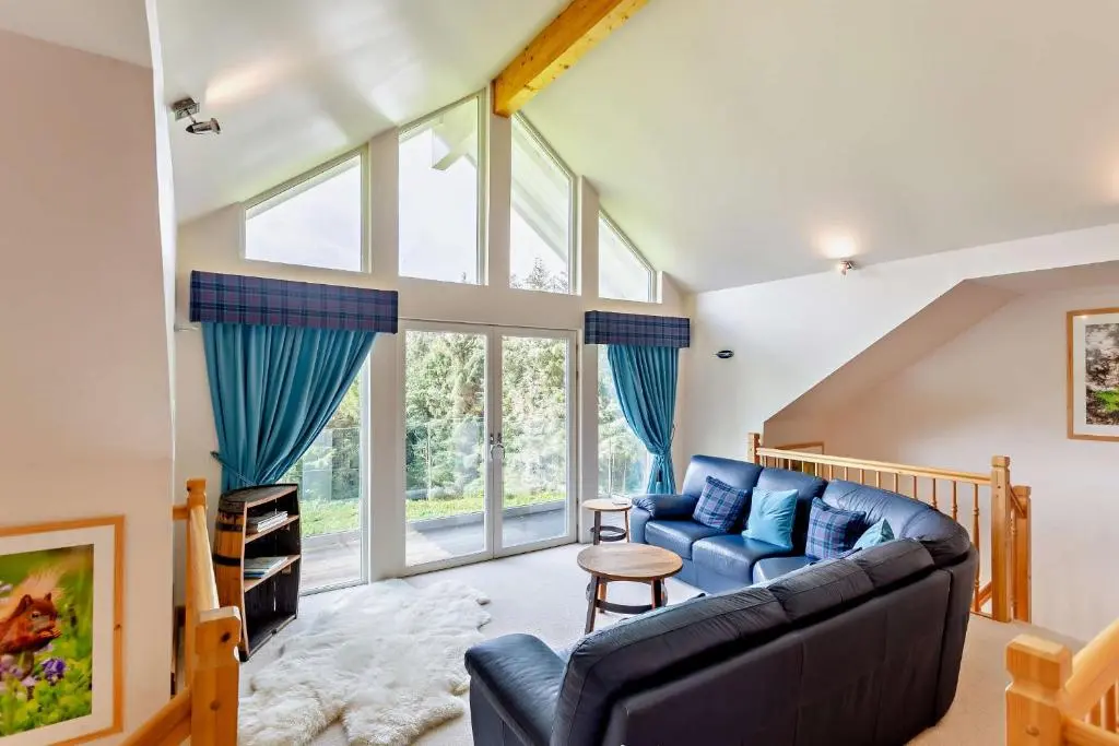a living room with a blue couch and some windows at Sealladh an Loch in Foyers