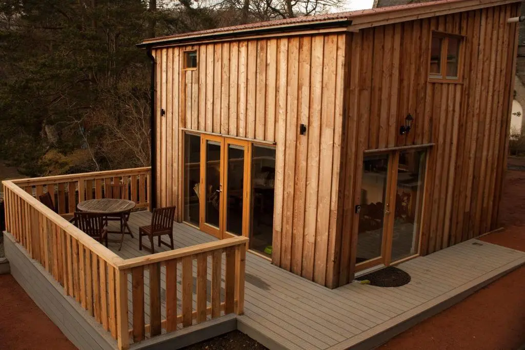 a wooden cabin with a table and chairs on a deck at Carn Na Drochaide in Braemar