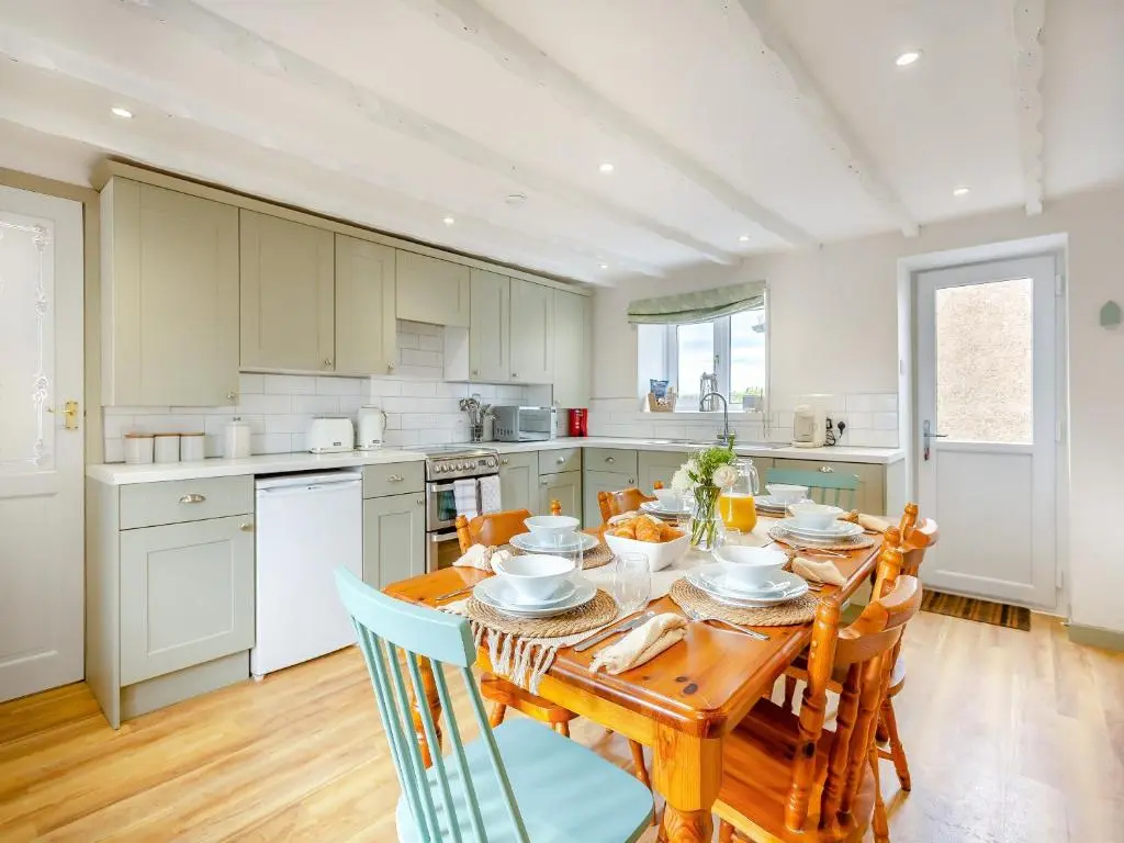 a kitchen with a wooden table and a kitchen with white appliances at Emerald Cottage in Burghead