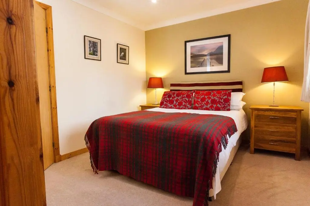a bedroom with a bed with a red and black blanket at Riverside Lodge Garden Apartment in Aviemore