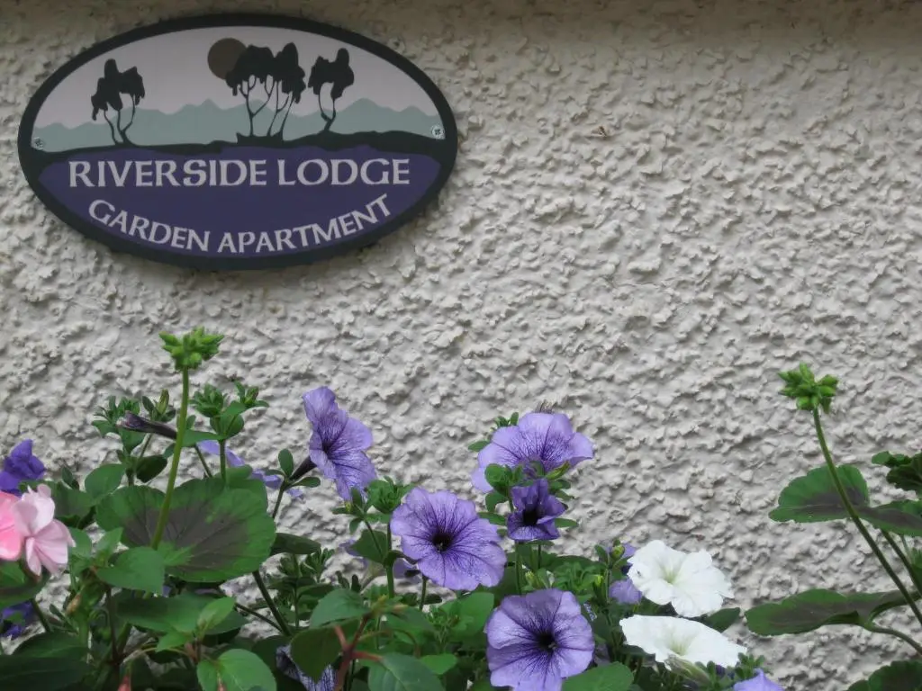 a sign on the side of a building with purple flowers at Riverside Lodge Garden Apartment in Aviemore