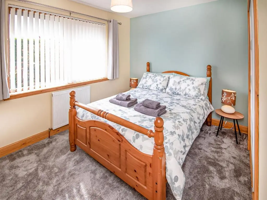 a bedroom with a wooden bed and a window at Beinn View House in Cononbridge