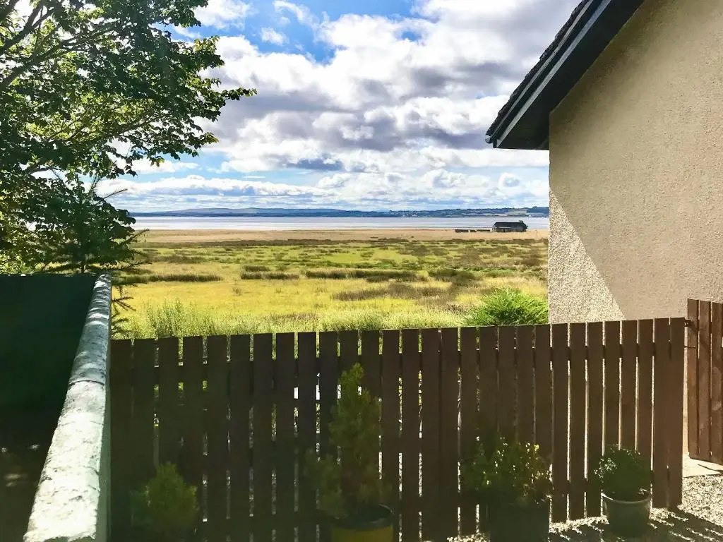 a fence with a view of the ocean from a house at Achnacarry Cottage in Evelix