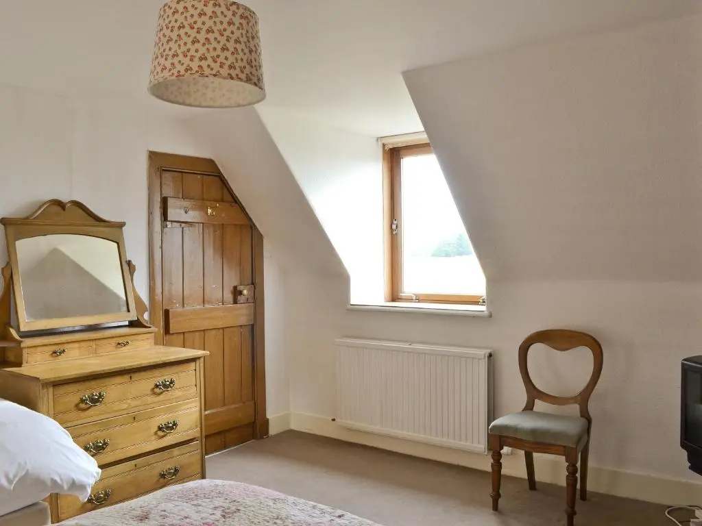 a bedroom with a dresser and a mirror and a chair at Old Post Office House in Knockbain