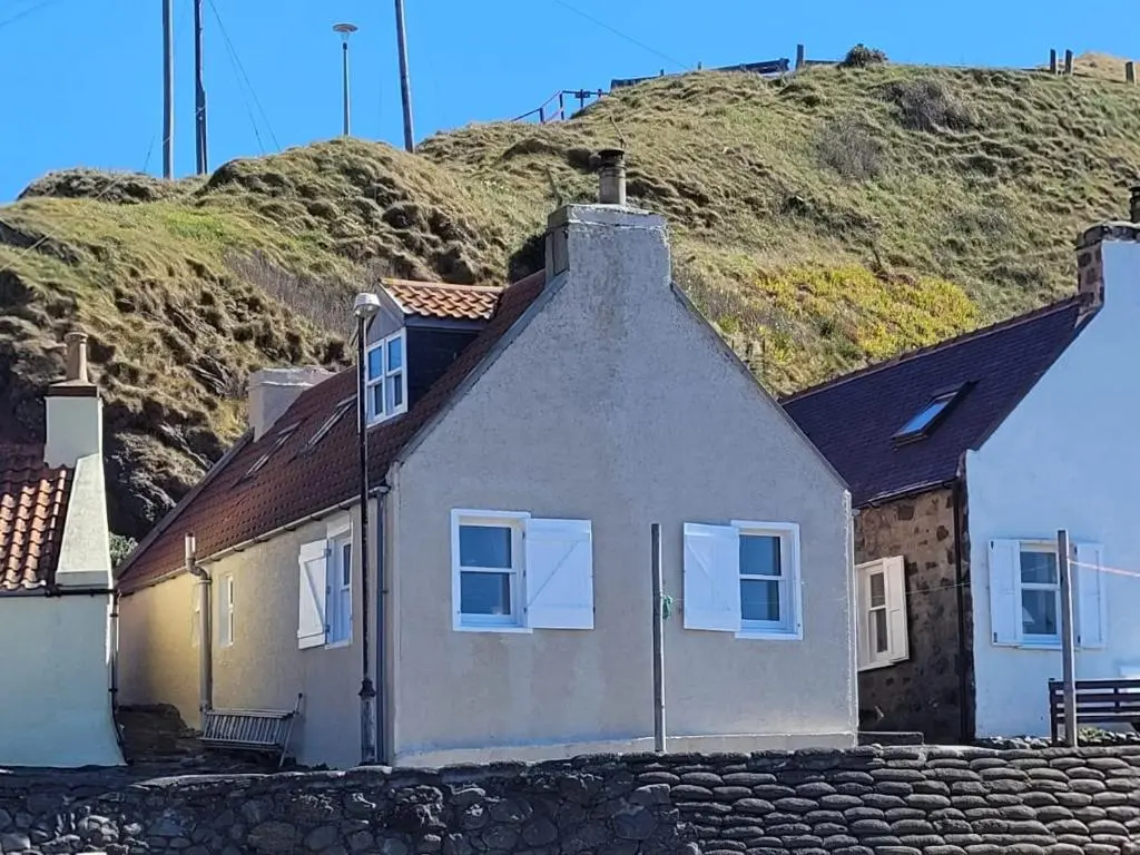 a white house with a hill in the background at Crovie Cottage in Gardenstown