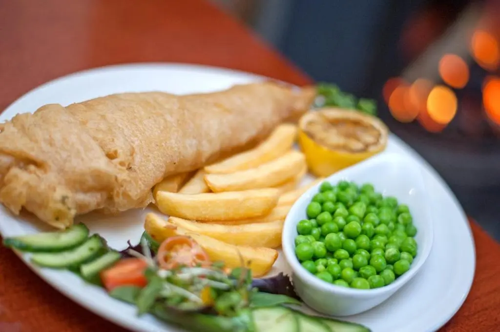 a plate of food with peas and a fish and chips at Nethybridge Hotel in Nethy Bridge