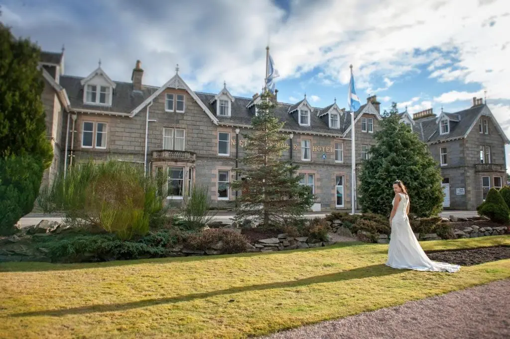 a bride standing in front of a large building at Nethybridge Hotel in Nethy Bridge
