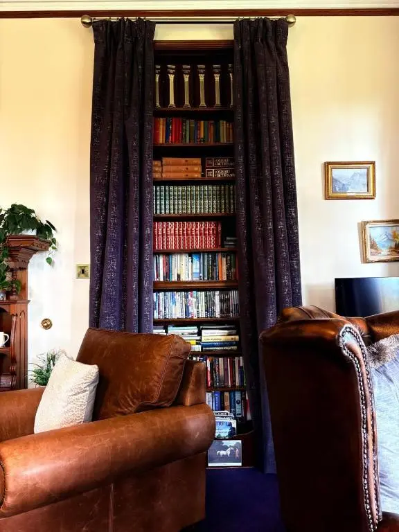 a living room with a couch and a book shelf filled with books at Dalrachney Lodge in Carrbridge