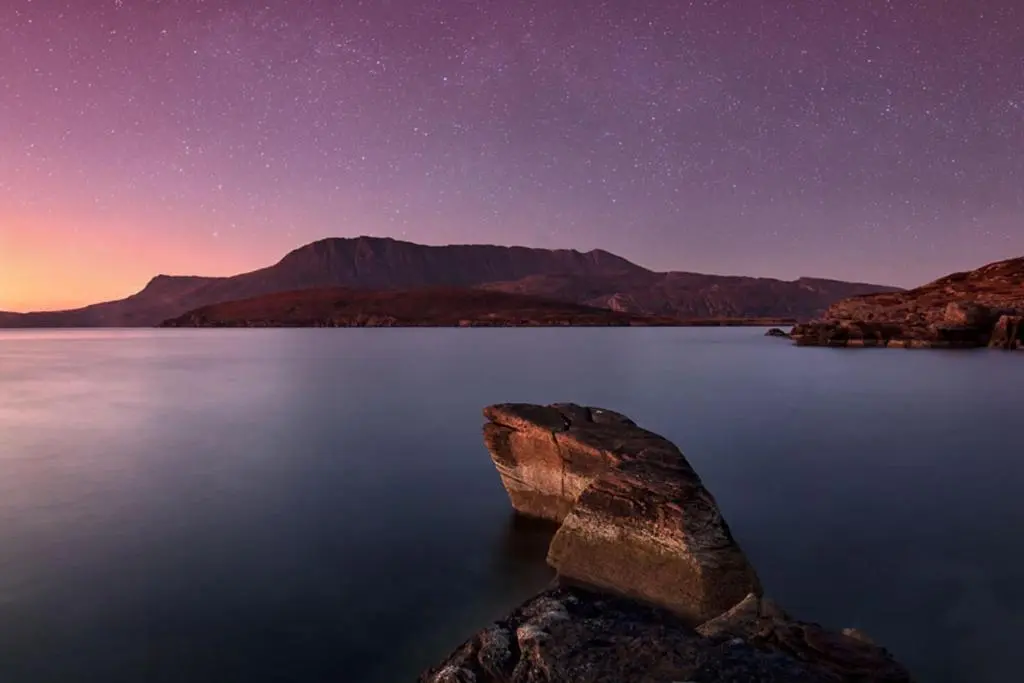 a starry night over a lake with a rock in the water at House - Sleeps 8 - Pets Ok - Parking in Ullapool