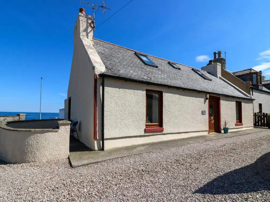 a white cottage with a red door on a gravel road at Jade Cottage in Macduff