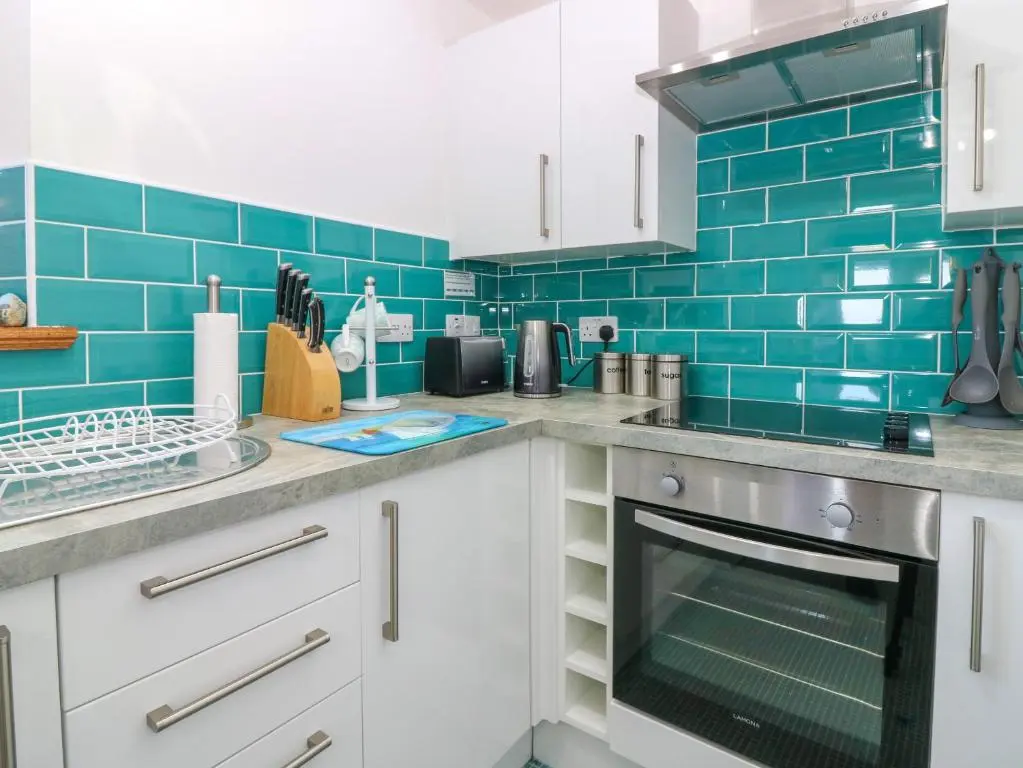a kitchen with white cabinets and blue tiles at Jade Cottage in Macduff