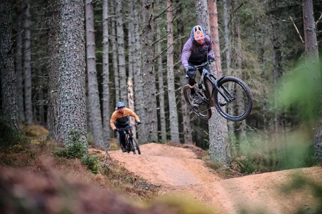 two people riding bikes on a dirt trail in the woods at Glenlivet by Wigwam Holidays in Tomintoul