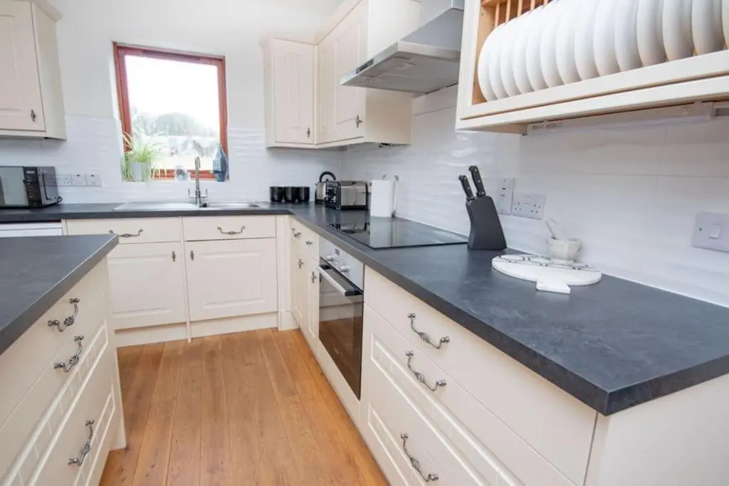 a kitchen with white cabinets and a black counter top at Grieves Cottage, near Dornoch in Dornoch