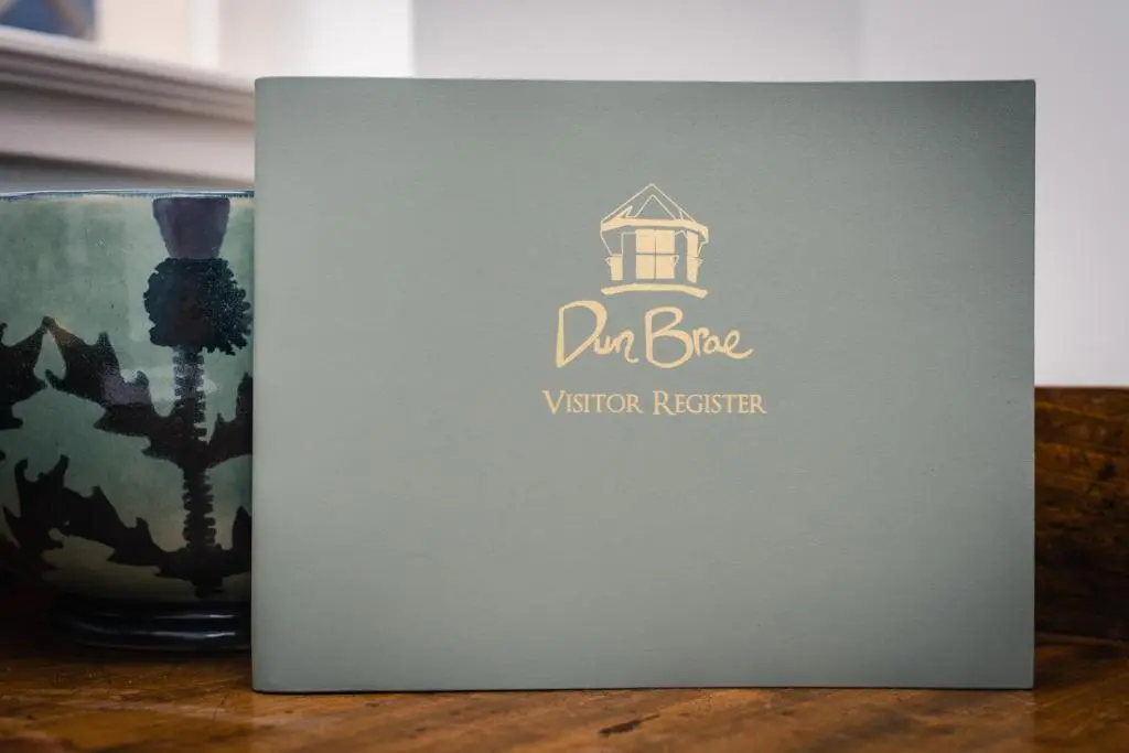 a sign that says d bite visitor register with a vase at Dun Brae Cottage in Dornoch