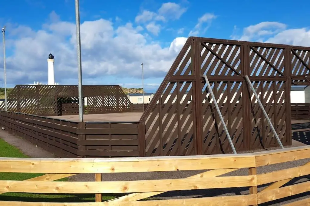 a wooden bridge with a lighthouse in the background at Coral Cove in Lossiemouth
