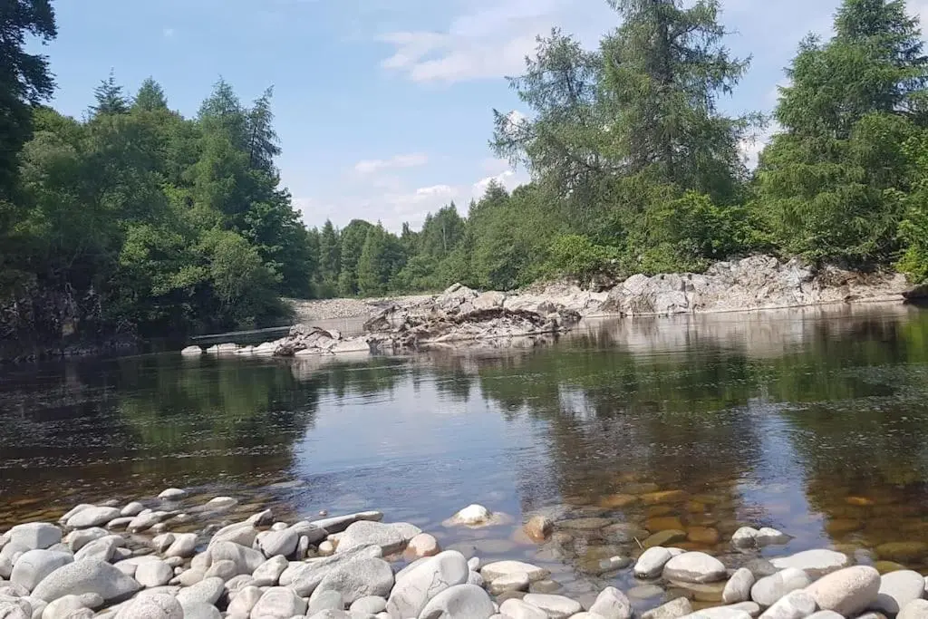 a river with rocks in the water and trees at Orchid lodge in Bridge of Tilt