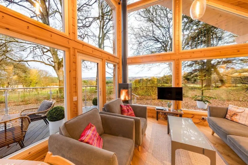 a large living room in a wooden house with windows at Cherry Tree Lodge in Inverness