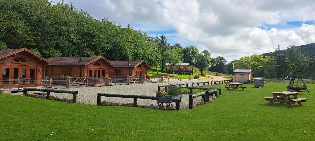 a log cabin with benches and tables in the grass at Cobblehouse Country Cabins no TRADE WORKERS in Inverkeithny