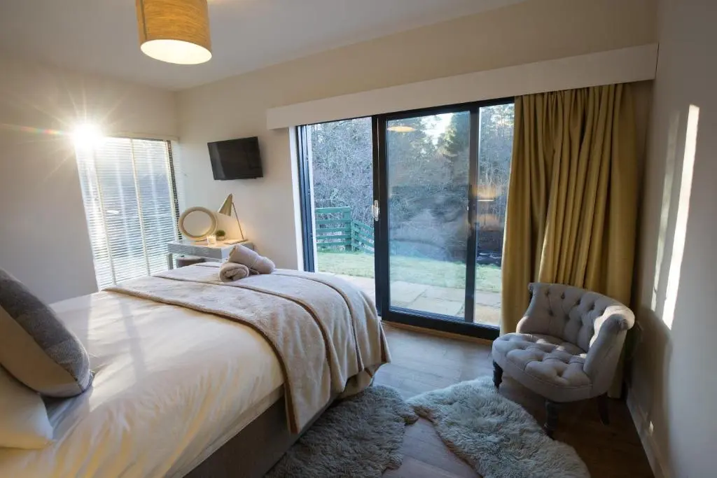 a bedroom with a bed and a chair and a window at Riverside Lodge - Seasgair Lodges in Nethy Bridge