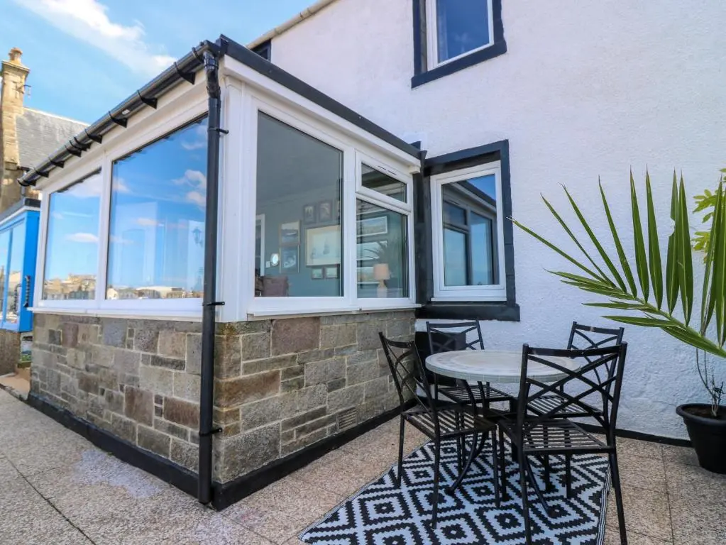 a patio with a table and chairs and windows at West Pier Cottage in Macduff