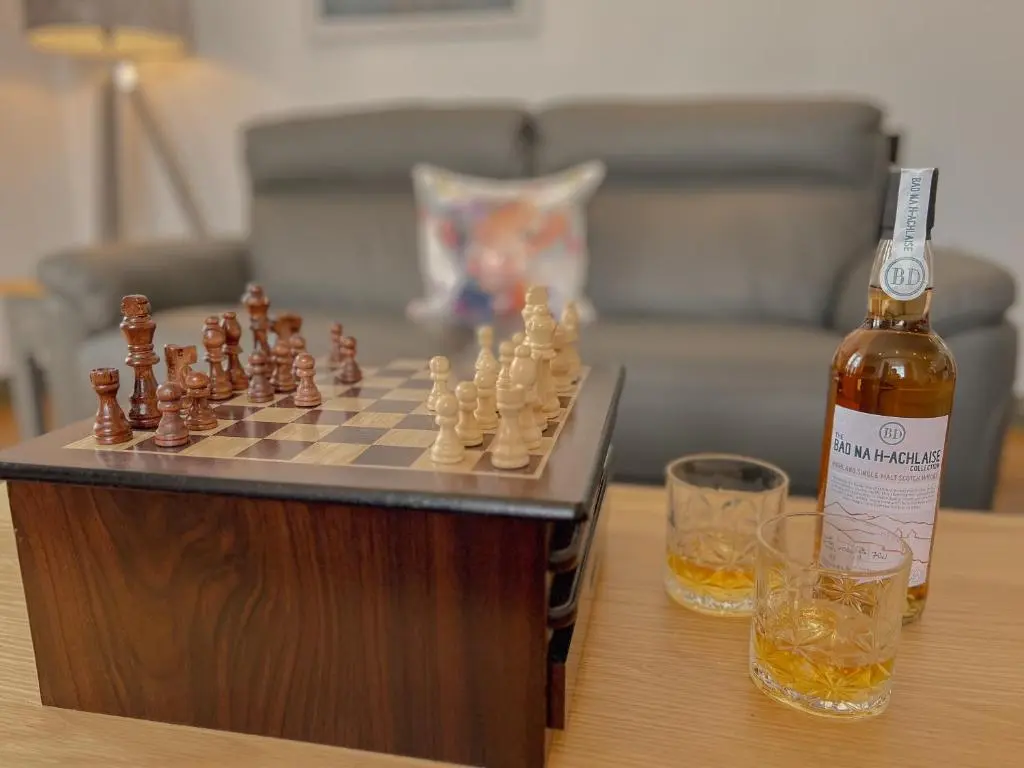 a bottle of beer next to a chess board and glasses at Loch Ness Gatehouse Apartments in Fort Augustus